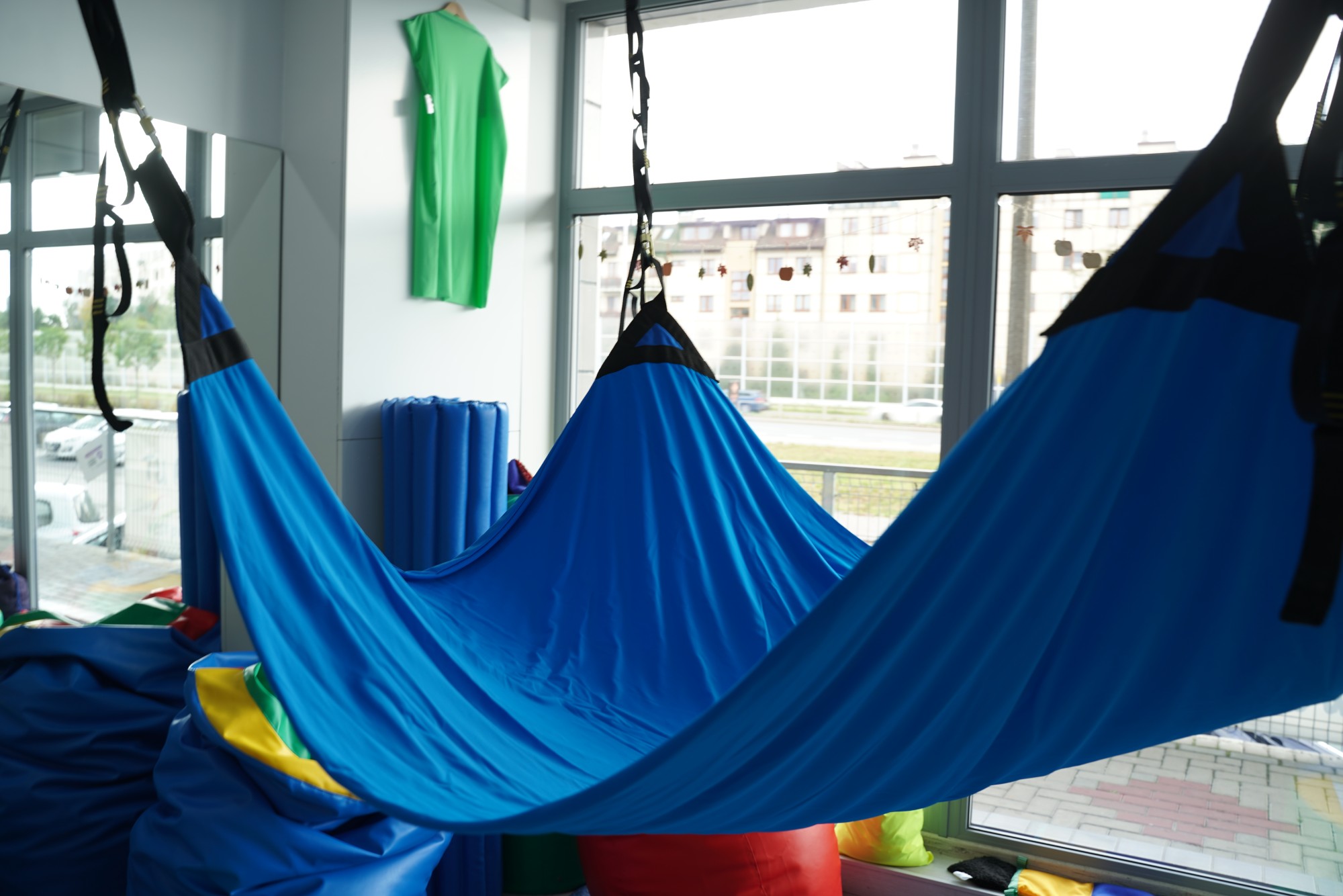 Zbliżenie na materiał lycra i jeden z zaczepów trampoliny sensorycznej; widoczna struktura tkaniny i taśmy wzmacniającej